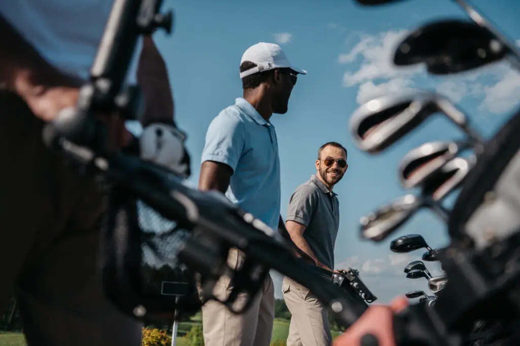 Two men smiling at each other with golf clubs in the foreground.
